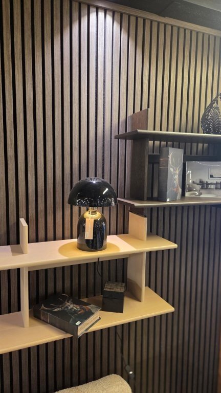 Svart bordslampa på hylla vid lamellvägg